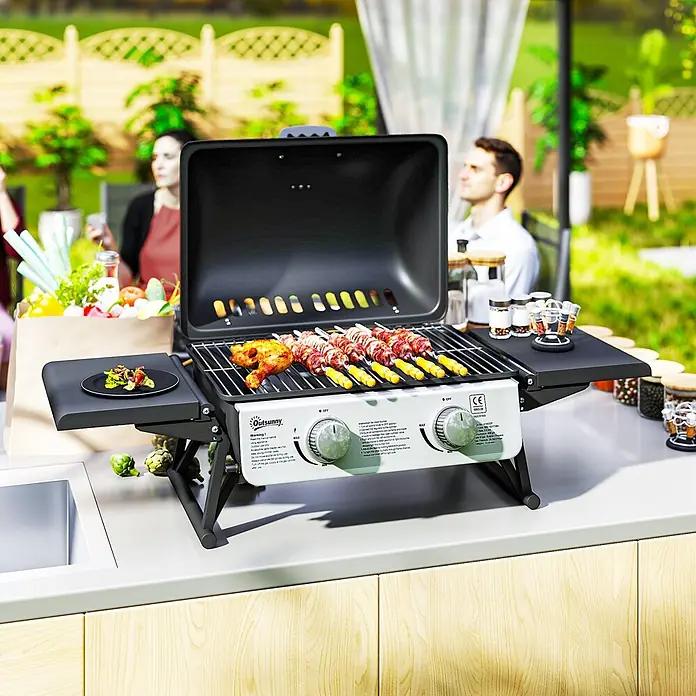 Outsunny Gasgrill - Anzahl Brenner: 2 Stk. - Tragbarer schwarz-weißer Gasgrill kocht Spieße und Hühnchen auf einer Theke im Freien, mit Personen im Hintergrund.