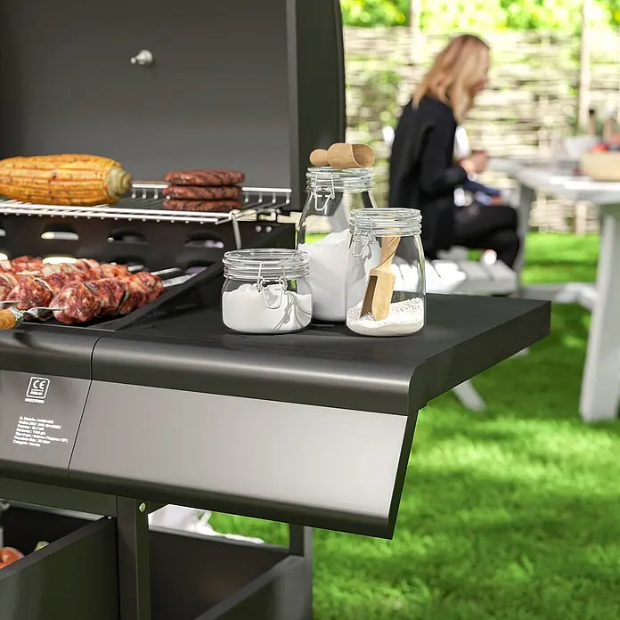 Outsunny Gasgrill - Anzahl Brenner: 4 Stk. - Ein schwarzer Grill mit Mais, Burgern und Spießen, Gewürzgläsern auf der Seitenablage, wird draußen im Garten verwendet.