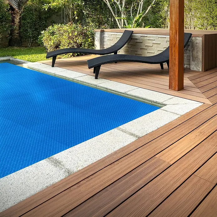 ECD Germany Solarabdeckplane Pool Solarfolie 400µm Solarplane Solarabdeckung Blau - Passend für: Rechteckpools, Aufstellpools, Swimmingpools, Material: Kunststoff - Braunes Verbundholz-Decking um einen Pool mit blauer Abdeckung und schwarzen Liegestühlen im Garten.