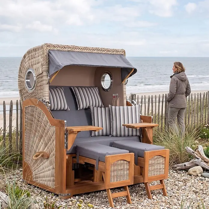 Mr. Deko Strandstuhl Strandkorb Düne Bullauge Teak PE Shell Dessin 544 - Teakholz. Polyrattan, Rückenlehne verstellbar, PE Shell, B x T x H: 125 x 80 x 170 cm - Geflochtener Strandkorb mit Holzrahmen, grauen Polstern und ausziehbaren Fußteilen, am Kiesstrand am Meer.