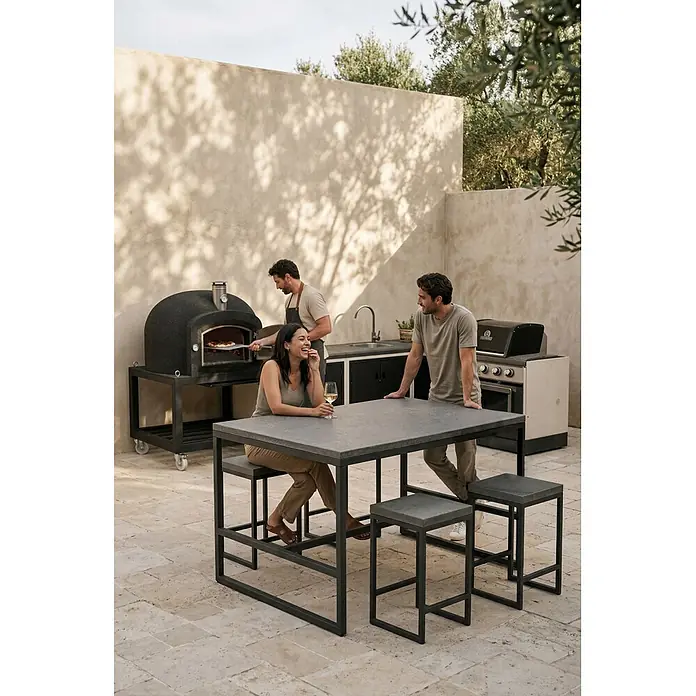 Tuozi Kitaway Outdoorküchen-Modul - Grau/Weiß, B x T x H: 100 x 100 x 65 cm - Menschen genießen eine Außenküche mit dunklem Pizzaofen, Grill und einem dunkelgrauen Tisch mit passenden Hockern.