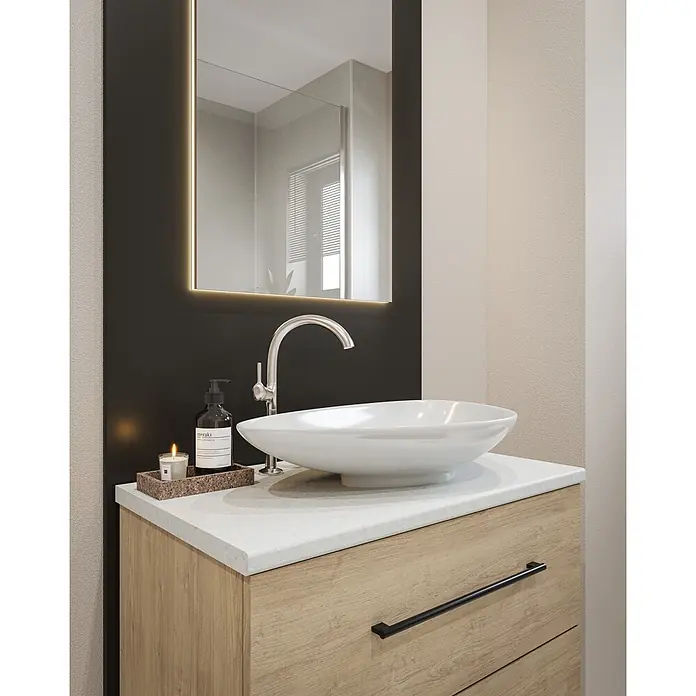 Wetwall Waschtischplatte Vanity HPL - 150 x 60 x 2,8 cm, Blanco Frost - Ein moderner Waschtisch mit hellem Holzunterschrank, weißer Arbeitsplatte, weißem Aufsatzwaschbecken und Chromarmatur. Ein beleuchteter Spiegel hängt darüber.