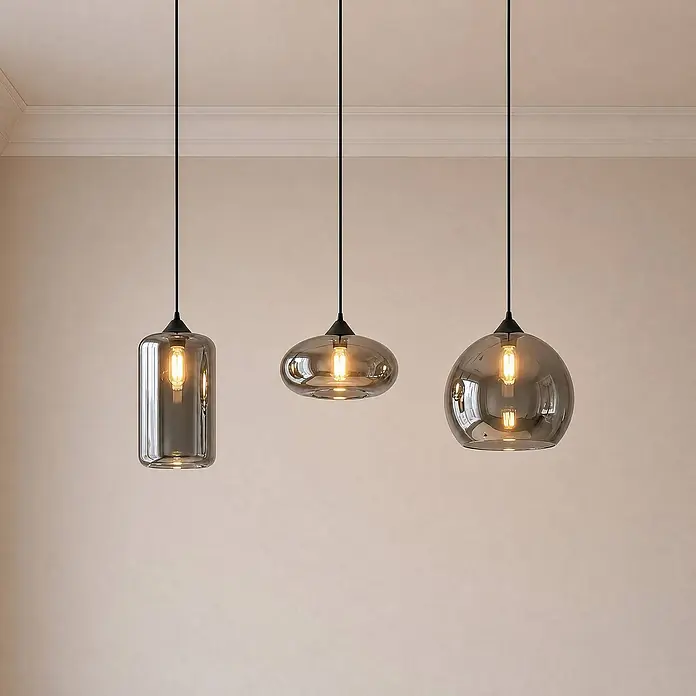 Lindby Pendelleuchte Marla - L x B x H: 102,5 x 28 x 28 cm, alu / grau / zink, rauchgrau, E27 - Drei Pendelleuchten mit Rauchglas-Schirmen in verschiedenen Formen, die glühende Edison-Birnen zeigen.
