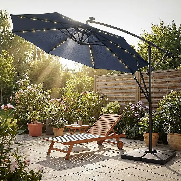 ML-Design Ampelschirm rund Gartenschirm UV50+ Sonnenschutz wasserabweisend 360° drehbar & neigbar - Blau, Durchmesser Bespannung: 300 cm - Dunkelblauer Ampelschirm mit LED-Beleuchtung und schwarzem Gestell, der eine Holzliege auf einer Terrasse beschattet.