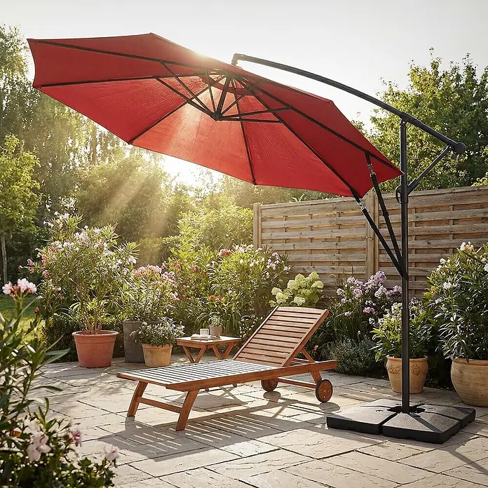 Ampelschirm Ø 300 cm rund in Rot aus Aluminium 360° drehbar -  - Ein roter Ampelschirm beschattet eine Holzliege und einen Beistelltisch auf einer sonnigen Terrasse.