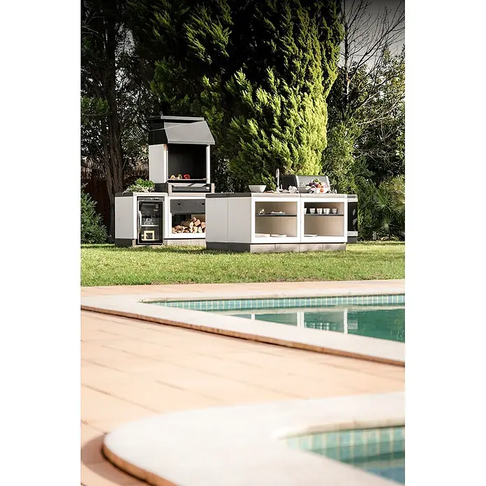 Tuozi Kitaway Holzkohlegrill - Grau/Weiß, B x T x H: 84 x 63 x 206 cm, Mehrstufige Höhenarretierung - Modulare Outdoor-Küche mit weißen und dunkelgrauen Einheiten, inklusive Grill, Spüle, Stauraum und Kühlschrank, in einem Garten neben einem Pool.