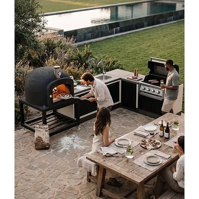 Tuozi Kitaway Outdoorküchen-Modul Seitenschrank - Grau/Weiß, B x T x H: 61 x 63 x 85 cm - Außenküche mit dunkelgrauem Pizzaofen, Grill und Spüle, von Leuten zum Kochen und Essen im Freien am Pool genutzt.