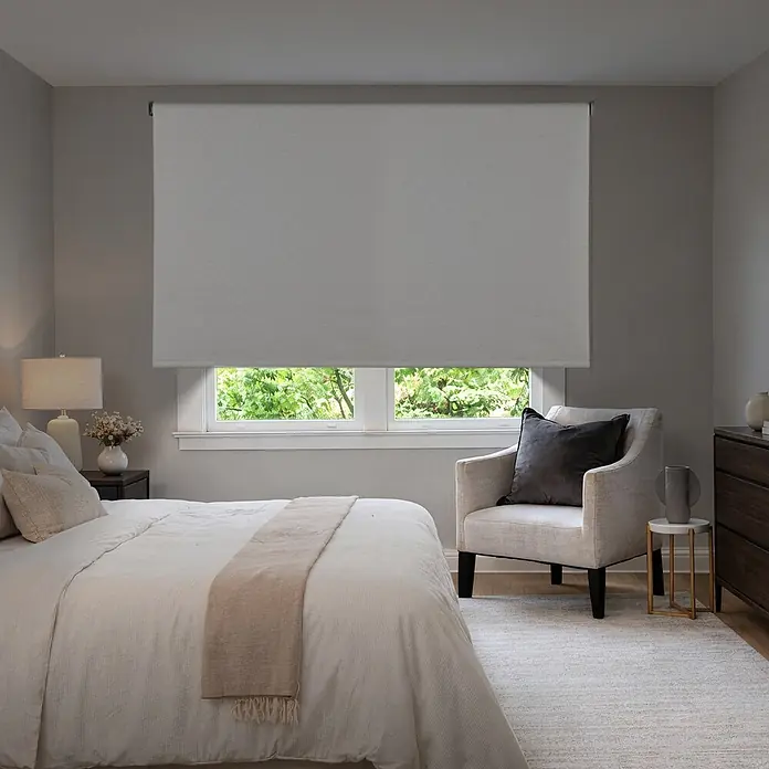 Estor enrollable opaco Scandi - An x Al: 140 x 250 cm, Lino - Una persiana enrollable gris que cubre parcialmente una ventana en un dormitorio, con árboles verdes visibles afuera.