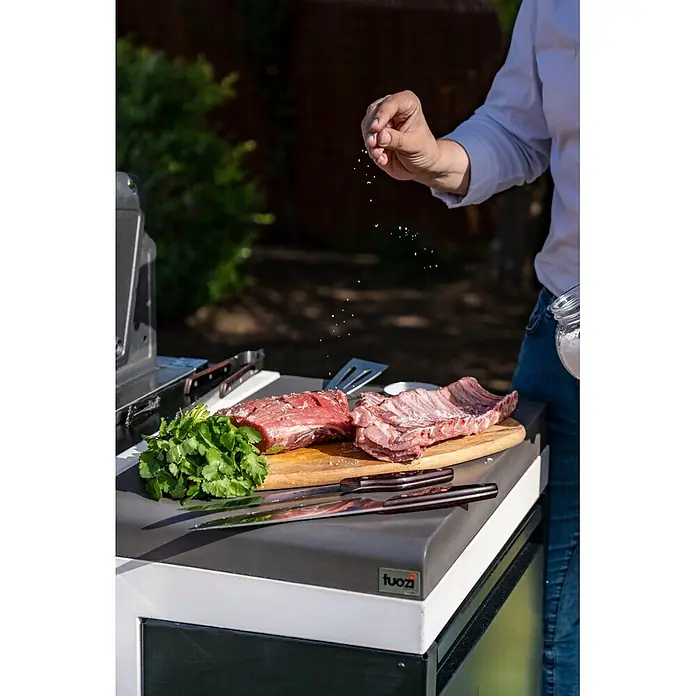 Tuozi Kitaway Outdoorküchen-Modul Abfalleimer - Grau/Weiß/Schwarz, B x T x H: 63 x 42 x 85 cm, Stahl - Dunkelgraue Arbeitsplatte eines Outdoorküchenmoduls. Eine Person würzt rohes Fleisch auf seiner Zubereitungsfläche.