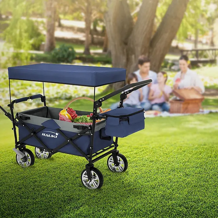 Hauki Bollerwagen Handwagen Transportwagen faltbar klappbar mit Bremse Dach und Tasche - L x B x H: 196 x 56 x 99 cm - Blauer Bollerwagen mit Dach und Kühltasche, gefüllt mit Picknickartikeln, in einem Park mit picknickender Familie.