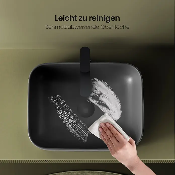 Emke Aufsatzwaschbecken CB09 - 605 x 380 mm, Hahnloch: Ohne, Ohne Überlauf, Dunkelgrau matt - Eine Hand reinigt ein schwarzes rechteckiges Waschbecken mit einem Tuch und Seife, was seine pflegeleichte Oberfläche zeigt.