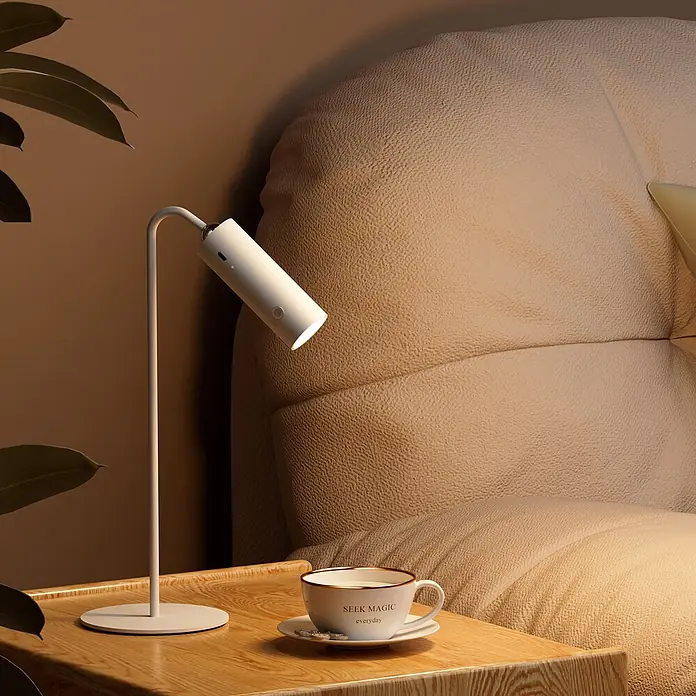 Emke LED-Tischleuchte -  - Weiße moderne Schreibtischlampe beleuchtet einen Holznachttisch und ein beiges Kopfteil.