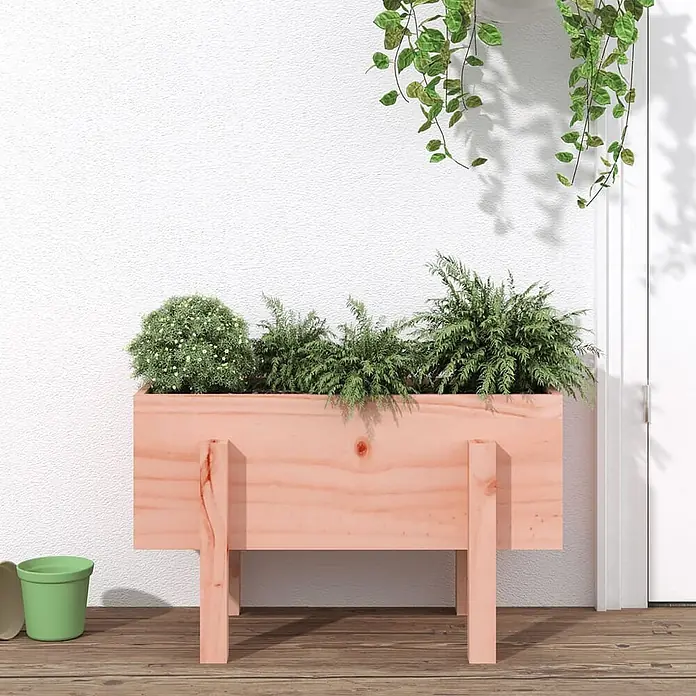 Furnicato Hochbeet - 30 x 62 x 38 cm, Holz, Natürliches Douglasie - Rechteckiger hellrosa Holz-Pflanzkasten auf Beinen, gefüllt mit verschiedenen Grünpflanzen, auf einer Holzterrasse.