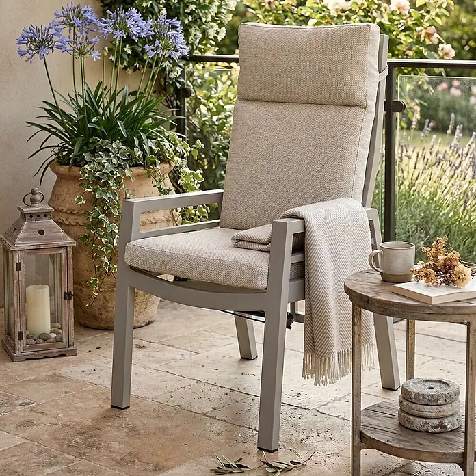 Bene Living Gartenstuhl-Set Sevilla - 2 Stk., Aluminium mit Textillene, beige - Grauer Gartenstuhl mit hellbeigen Kissen und einer gemusterten Decke auf einer Terrasse mit Pflanzen und einem Beistelltisch.