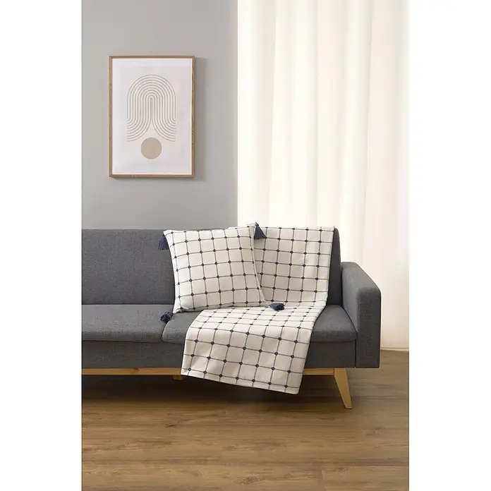 Colcha Edna - 260 x 240 cm, 65% algodón y 35% poliéster, Blanco - Cojín y manta blancos con patrón de cuadrícula azul y borlas, sobre un sofá gris.