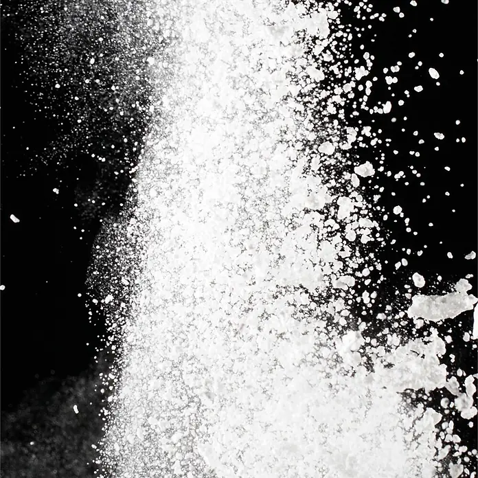 SanDesign Acryl-Verbundplatte - 100 x 250 cm, Bubbly Waterfall - Weißes, körniges Pulver unterschiedlicher Größe vor dunklem Hintergrund.