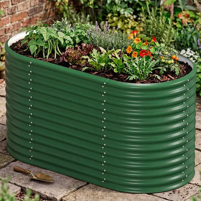 Vitavia Hochbeet Terra 858 - 162 x 82 x 85,8 cm, Zincalume®, Seegras - Grünes, gewelltes ovales Metall-Hochbeet, gefüllt mit Pflanzen (Bohnen, Kräuter), auf Steinplatten, daneben eine Schaufel.