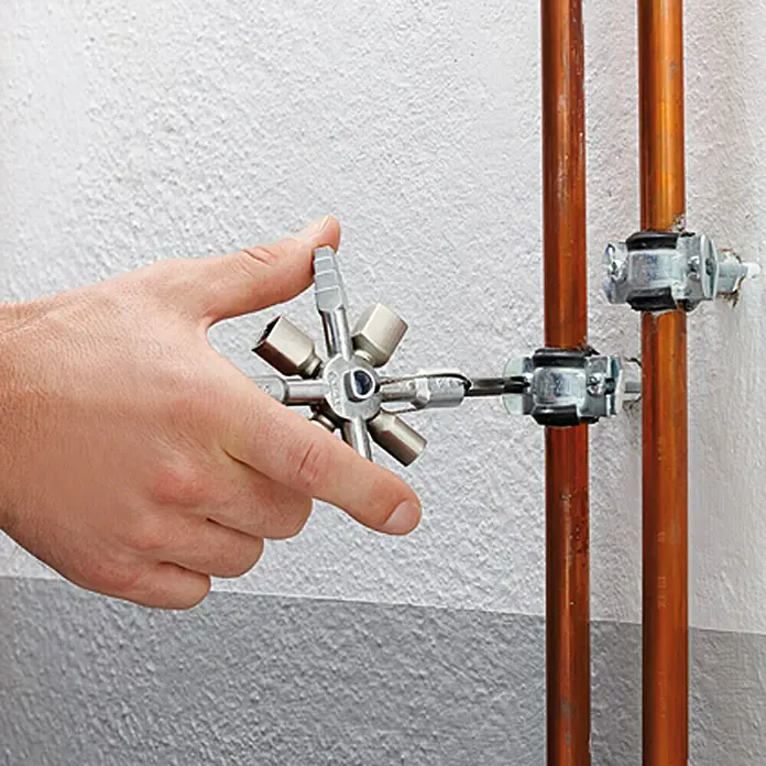 Knipex Universal-Schlüssel Twin Key - 10 Werkzeuge - Ein Mann bedient mit einem Multifunktionsschlüssel eine Rohrschelle an zwei Kupferrohren vor einer weißen Wand.