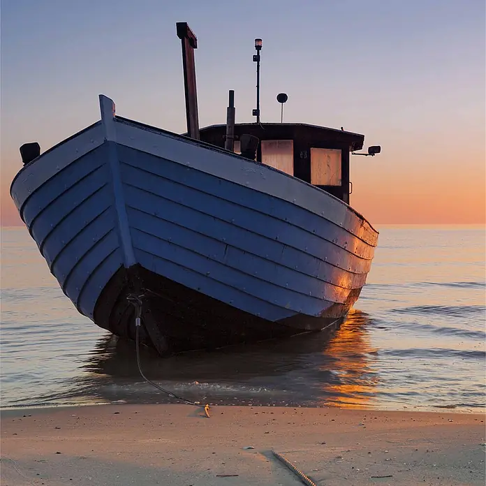 SanDesign Alu-Verbundplatte - 100 x 250 cm, Boat on Sea - Blaues Holzfischerboot am Sandstrand mit im Wasser spiegelndem Sonnenuntergang.
