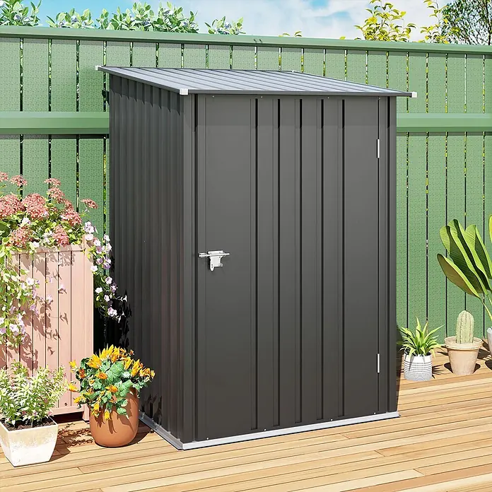 Outsunny Gerätehaus - Außenbreite inkl. Dachüberstand: 100 cm, Außentiefe inkl. Dachüberstand: 103 cm, Stahl, Dunkelgrau - Dunkelgraues Metall-Gerätehaus auf Holzterrasse, umgeben von Pflanzen und grünem Zaun, zur Gartenaufbewahrung.