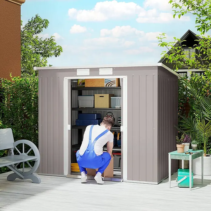 Outsunny Gerätehaus - Außenbreite inkl. Dachüberstand: 213 cm, Außentiefe inkl. Dachüberstand: 130 cm, Stahl, Hellgrau - Grauer Metall-Gartenschuppen, in dem eine Person Gegenstände sortiert.