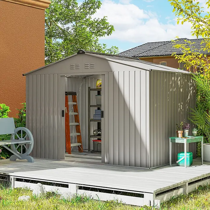 Outsunny Gerätehaus - Außenbreite inkl. Dachüberstand: 277 cm, Außentiefe inkl. Dachüberstand: 195 cm, Stahl, Grau - Graues Gartenhaus aus Metall mit offener Tür, das innen Regale und eine Leiter zeigt, auf einer Holzterrasse im Garten.