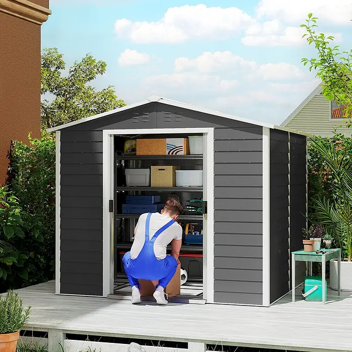 Outsunny Gerätehaus - Außenbreite inkl. Dachüberstand: 240 cm, Außentiefe inkl. Dachüberstand: 206 cm, Stahl, Dunkelgrau - Mann verstaut Gegenstände in einem dunkelgrauen Metall-Gartenschuppen auf einer Holzterrasse.