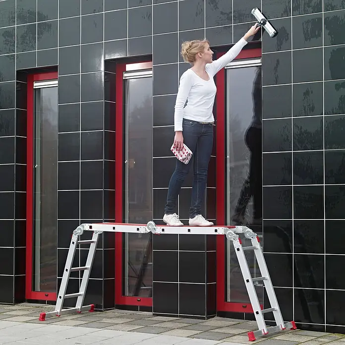 Altrex Mehrzweckleiter Vielzweckleiter Varitrex Plus 4x3 Sprossen - Anzahl Tritte: 3 Stk., Arbeitshöhe: 4.300 m, Aluminium - Eine Frau auf einer silber-roten Mehrzweckleiter, als Arbeitsplattform genutzt, beim Fensterputzen.