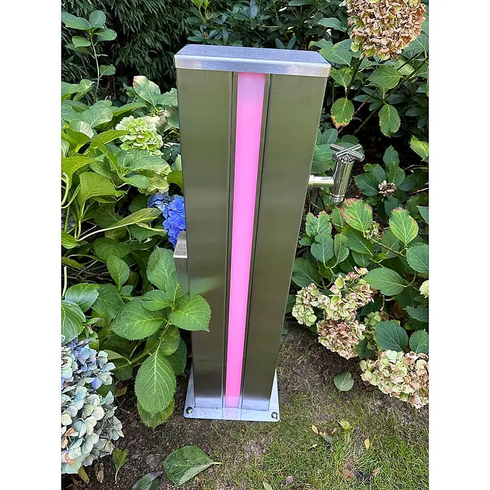 Ideal Eichenwald Pooldusche Modell 71 Multifunktionsstele LED beleuchtet - Edelstahl - Edelstahl-Gartenwasserzapfsäule mit vertikalem pinkfarbenem LED-Streifen und Wasserhahn, umgeben von Hortensien.