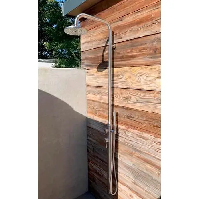Ideal Eichenwald Pooldusche Modell 70 Gartendusche Juist wandmontiert - Edelstahl - Silberne Außendusche mit Regenbrause und Handbrause, an rustikaler Holzwand neben einer Betonabtrennung montiert.