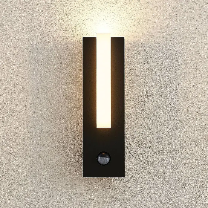 Lucande Außenwandleuchte Virgalia - schwarz, IP54 - Schwarze Außenwandleuchte mit weißem Leuchtstreifen und integriertem Bewegungsmelder, an strukturierter Wand montiert.