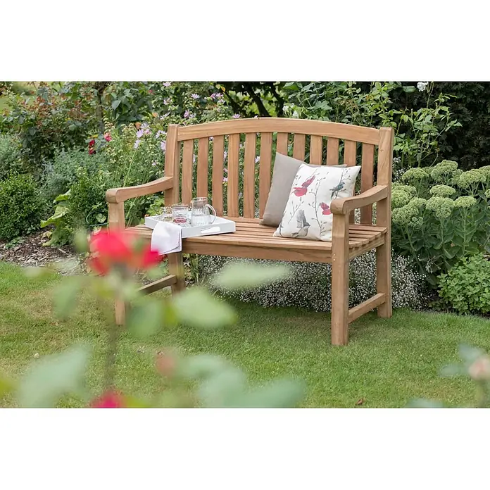 Bene Living Gartenbank Swindon - Teakholz, Natur - Eine Gartenbank aus Naturholz mit Kissen und einem Tablett mit Getränken.