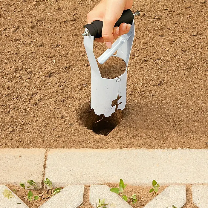 Gardol Plantador para bulbos - 80 mm, Negro/Plateado - Primer plano de una plantadora de bulbos blanca que se utiliza en el suelo para cavar un hoyo. Herramienta de jardinería en acción.