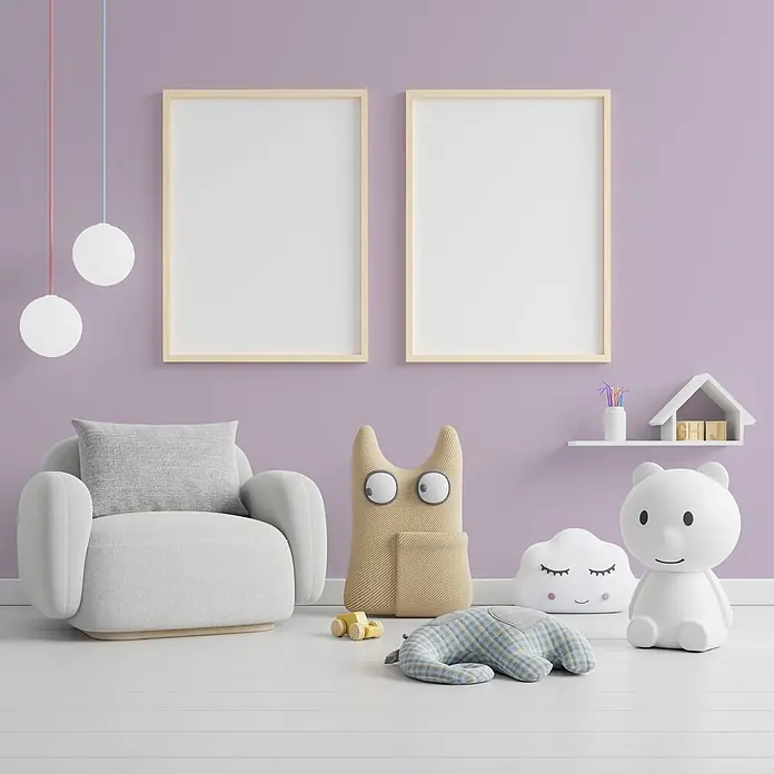 Tadessi Wandfarbe Blütenholz - Violett, Matt, 1 l - Ein verspieltes Kinderzimmer mit hellgrauem Sessel, zwei leeren Bilderrahmen, Pendelleuchten und diversen Spielzeugen.