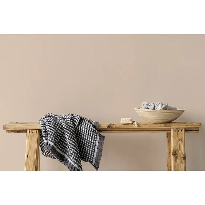 Tadessi Wandfarbe Biskuitbeige - Beige, Matt, 2,5 l - Strukturiertes grau-weißes Handtuch auf Holzbank, mit Holzschale mit gerollten Handtüchern und Bürste.