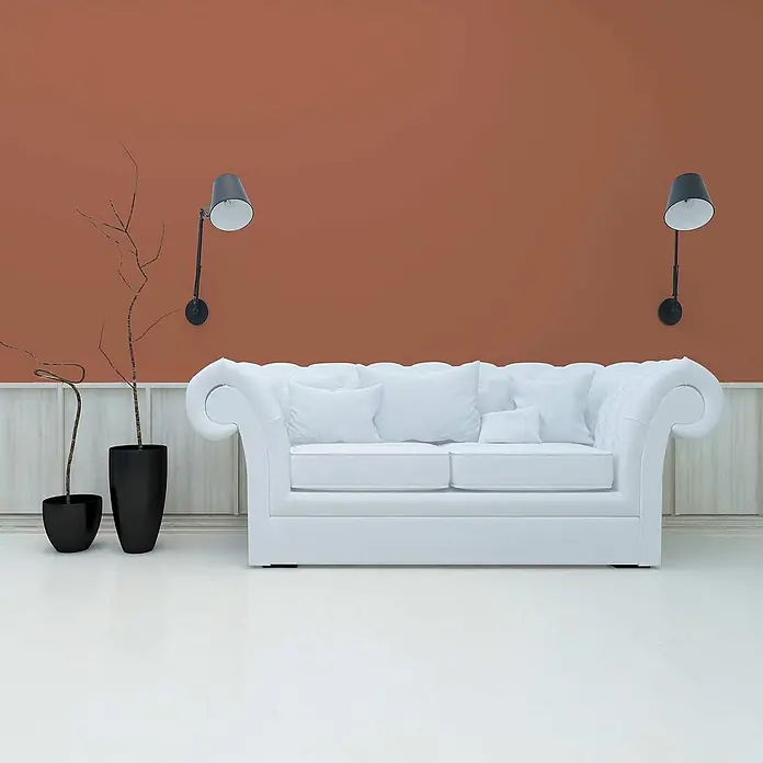 Tadessi Wandfarbe Aprikose - Rot, Matt, 5 l - Ein weißes Chesterfield-Sofa mit Zierarmlehnen steht in einem Raum mit oranger Wand, flankiert von zwei schwarzen Wandleuchten.