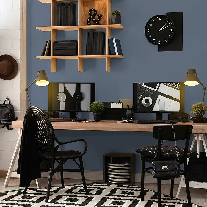 Tadessi Wandfarbe Taubenblau - Blau, Matt, 2,5 l - Ein modernes Heimbüro mit Holzschreibtisch, zwei schwarzen Stühlen und Doppelmonitoren vor einer blauen Wand.