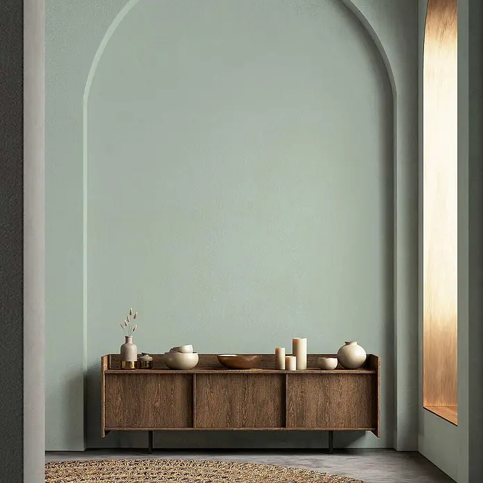 Tadessi Wandfarbe Eukalyptus - Grün, Matt, 5 l - Holz-Sideboard mit Schiebetüren, dekoriert mit minimalistischer Keramik vor einer hellgrünen Bogenwand.