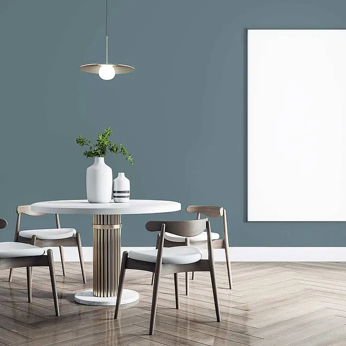 Tadessi Wandfarbe Mokka - Blau, Matt, 5 l - Modernes Esszimmer mit einem runden weißen Tisch mit goldener geriffelter Basis, umgeben von vier Holzstühlen mit hellen Polstern, unter einer Messing-Pendelleuchte.