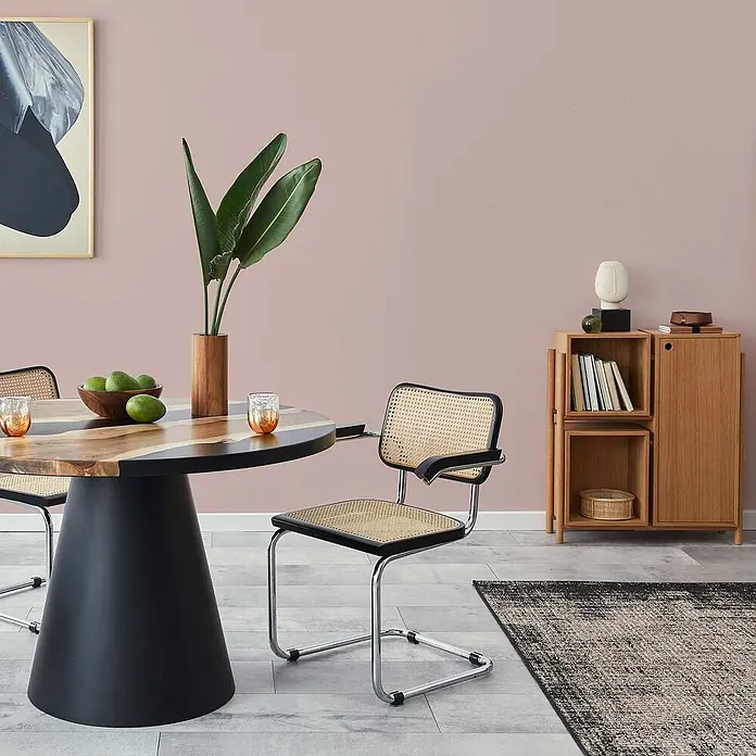 Tadessi Wandfarbe Tauperosa - Rosa, Matt, 5 l - Ein Esszimmer mit einem runden Holztisch, Korbstühlen mit schwarzen Rahmen und einem modularen Holzschrank.