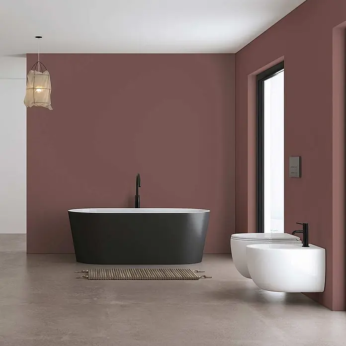 Tadessi Wandfarbe Zimt - Braun, Matt, 2,5 l - Ein modernes Bad mit schwarzer freistehender Badewanne, wandhängendem WC und Bidet in Weiß, vor rotbraunen Wänden.