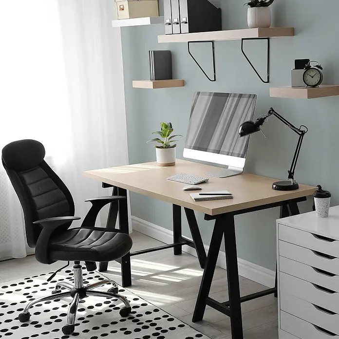 Tadessi Wandfarbe Toffee - Blau, Matt, 5 l - Ein modernes Home-Office mit hellem Holzschreibtisch, schwarzem Ergonomiestuhl, Computer und schwebenden Regalen an einer hellblauen Wand.