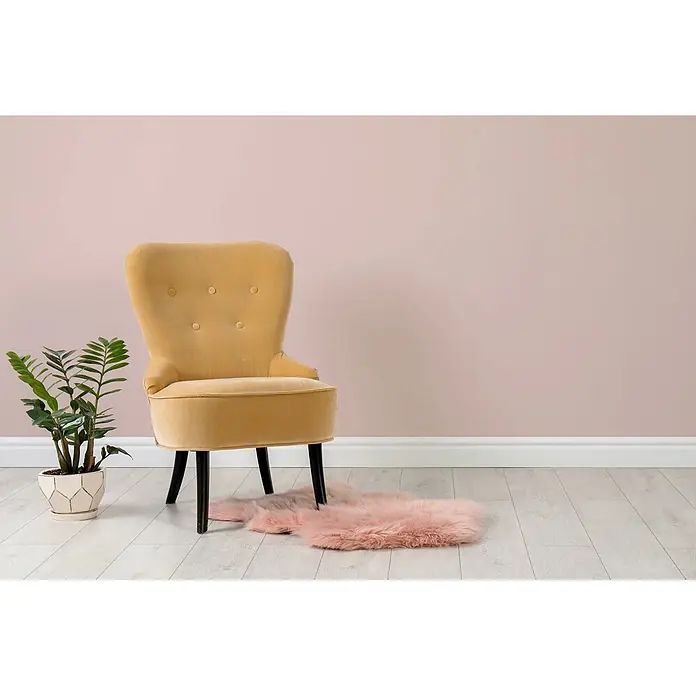 Tadessi Wandfarbe Rosenquarz - Beige, Matt, 2,5 l - Senfgelber Samtsessel mit Knopfheftung, weichem rosa Teppich und einer grünen Topfpflanze.