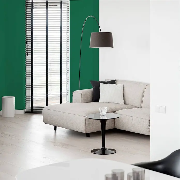 Tadessi Wandfarbe Dschungelgrün - Grün, Matt, 1 l - Bogenstehlampe mit dunkelgrauem Schirm, neben einem beigefarbenen Sofa in einem modernen Wohnzimmer platziert.