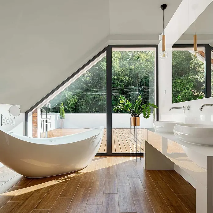 Tadessi Wandfarbe Khaki - Grau, Matt, 5 l - Modernes Badezimmer mit eleganter, weißer freistehender Badewanne, Doppelwaschtisch und großen Fenstern mit Waldblick.