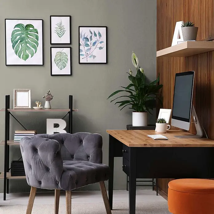 Tadessi Wandfarbe Khaki - Grau, Matt, 5 l - Modernes Heimbüro mit Holz- und schwarzem Schreibtisch, grauem Samtsessel und Regalen, dekoriert mit Pflanzen und Kunst.