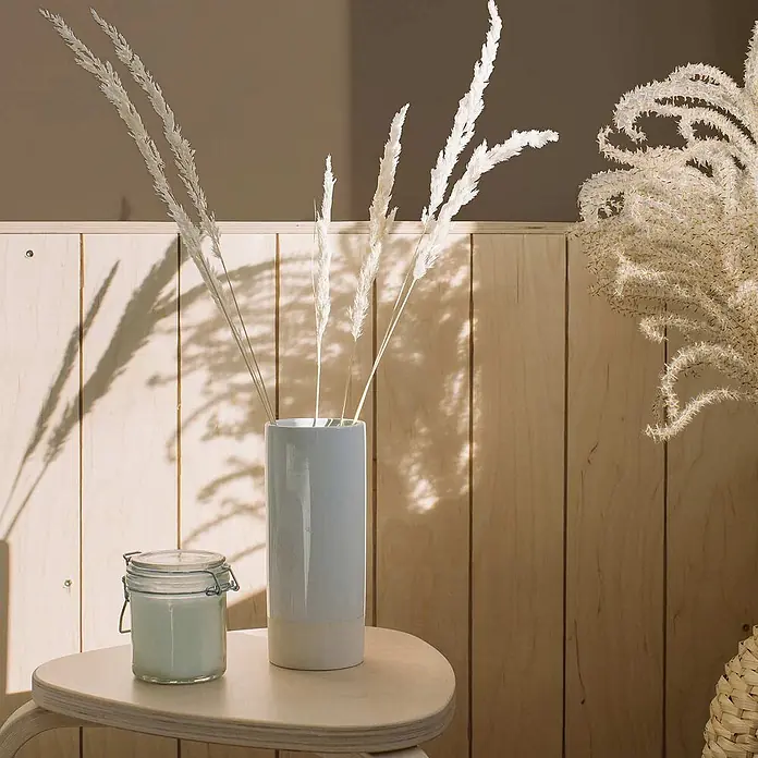 Tadessi Wandfarbe Mandelbraun - Braun, Matt, 1 l - Weiße Keramikvase mit getrocknetem Pampasgras, einem Glasgefäß und einem hellen Holztisch in sonniger Umgebung.