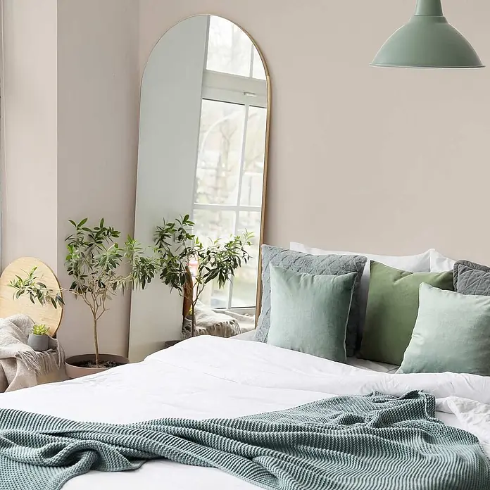 Tadessi Wandfarbe Eierschale - Creme, Matt, 2,5 l - Modernes Schlafzimmer mit einem großen Bogenspiegel, einem Bett mit salbeigrüner Strickdecke und passenden Kissen.