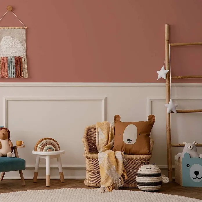 Tadessi Wandfarbe Rosenholz - Rot, Matt, 1 l - Gemütliches Kinderzimmer mit Korbstuhl, Bärenkissen, Regenbogenspielzeug und Wolken-Wandbehang an rosa Wand.