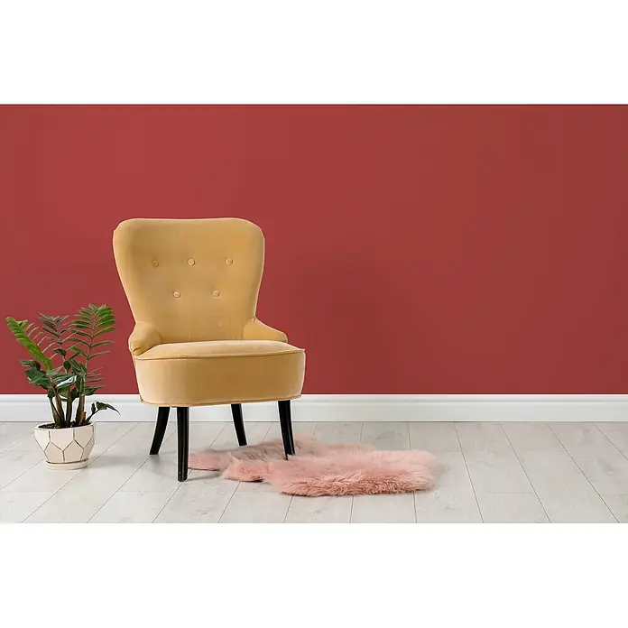 Tadessi Wandfarbe Cherry Rot - Rot, Matt, 5 l - Ein gelber Samtsessel mit schwarzen Beinen und getufteter Rückenlehne steht auf hellem Boden vor einer roten Wand, neben einer Pflanze und einem rosa Teppich.